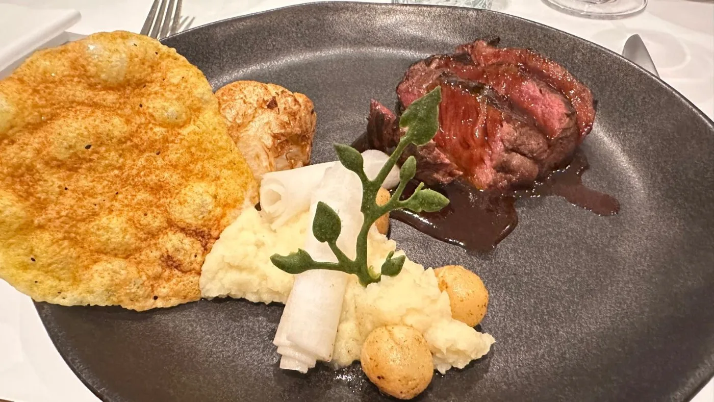 Voorbeeld van Rundstoof, gevogelte of lam met romige pastinaak-Parmazaanpuree, gebrande bloemkoolschijfjes, knolselderijbolletjes en gegrilde rettichtorentjes, afgewerkt met witlofblaadjes, een krokantje van Parmazaanse kaas en een verfijnde venkeljus, gegarneerd met cress