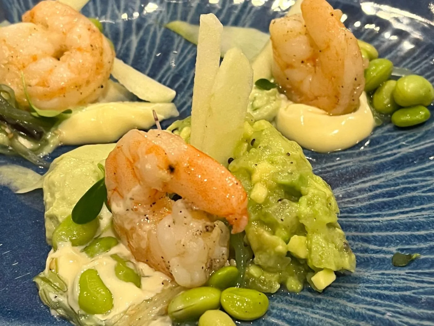 Voorbeeld van Garnalencocktail met avocado-crème, frisse komkommer, tartaar van kiwi en avocado, meloenbolletjes en sojabonen, afgegarneerd met Granny Smith-appel, een limoengrasdressing en cress